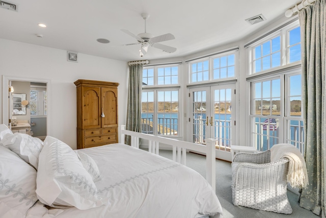 carpeted bedroom featuring a water view, access to outside, visible vents, and french doors