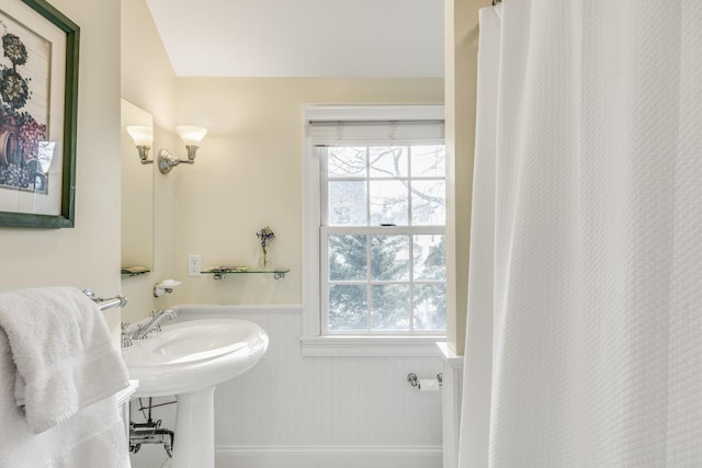 full bath with a shower with shower curtain, plenty of natural light, and wainscoting