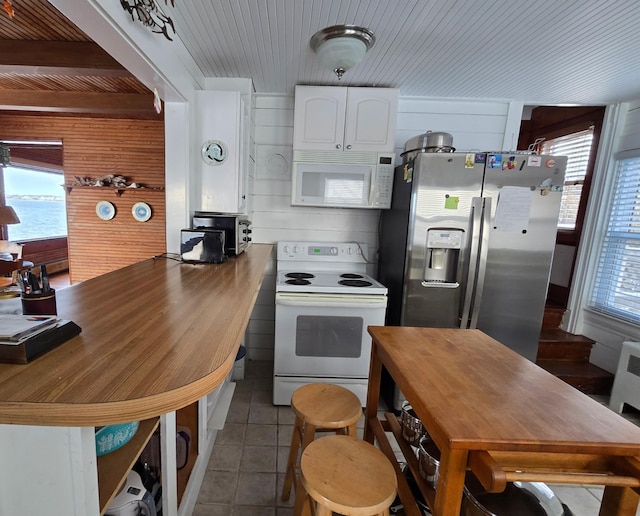 kitchen with white cabinetry, white appliances, light tile patterned floors, and wooden walls