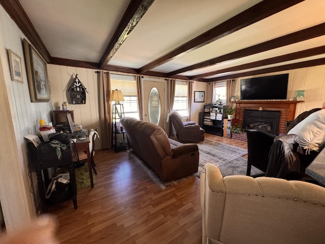 living area with beam ceiling, a brick fireplace, and wood finished floors