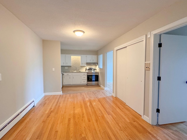 unfurnished living room featuring baseboard heating, a textured ceiling, sink, and light wood-type flooring