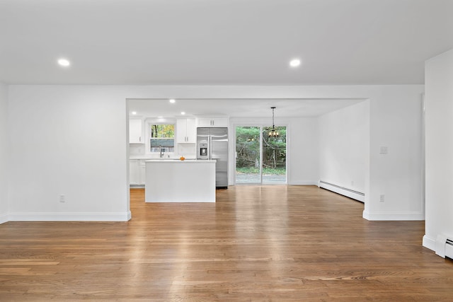 unfurnished living room featuring light hardwood / wood-style flooring, baseboard heating, and an inviting chandelier