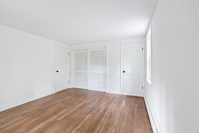 unfurnished bedroom featuring hardwood / wood-style flooring, multiple windows, and a baseboard heating unit