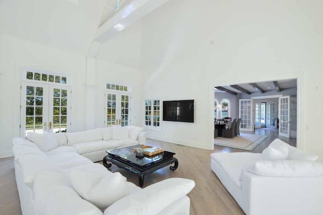 living room featuring french doors, light hardwood / wood-style floors, a high ceiling, and beamed ceiling