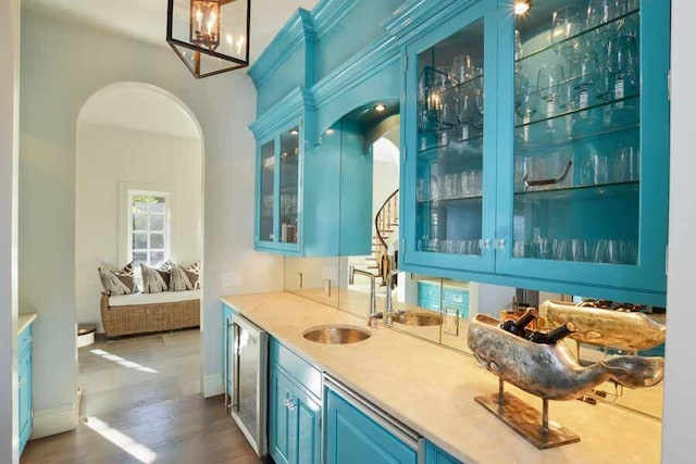 bar featuring dishwashing machine, sink, dark hardwood / wood-style floors, and blue cabinets