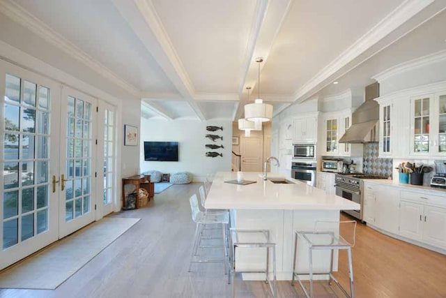 kitchen with sink, white cabinetry, appliances with stainless steel finishes, pendant lighting, and wall chimney range hood