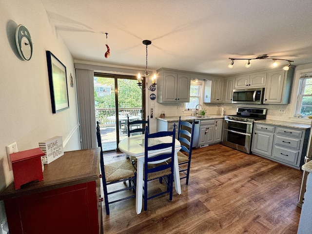 kitchen with stainless steel appliances, backsplash, dark hardwood / wood-style floors, gray cabinets, and hanging light fixtures