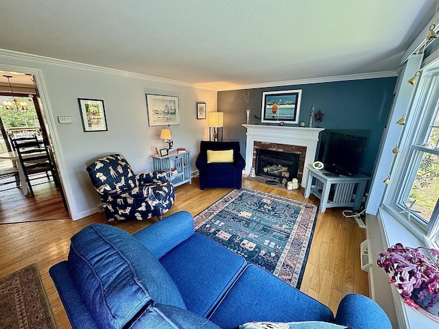 living room with a brick fireplace, wood-type flooring, ornamental molding, and a chandelier