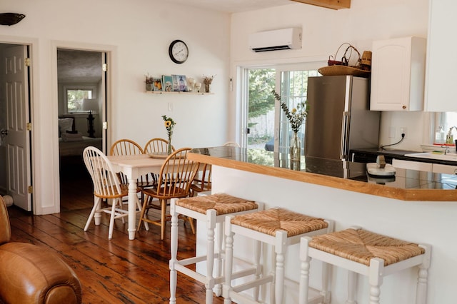 115 Rte 28, West Harwich, MA 02671 - kitchen with a kitchen bar, a wall unit AC, freestanding refrigerator, dark wood-style floors, and white cabinets