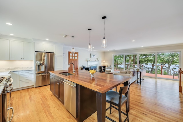 kitchen featuring a sink, white cabinets, open floor plan, appliances with stainless steel finishes, and a center island with sink