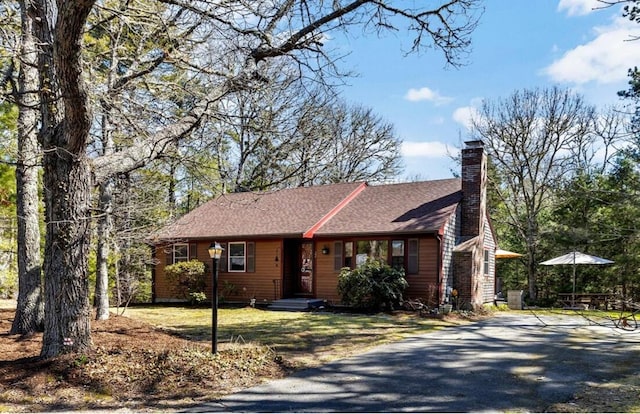 view of front of house featuring roof with shingles, a chimney, driveway, and a front lawn