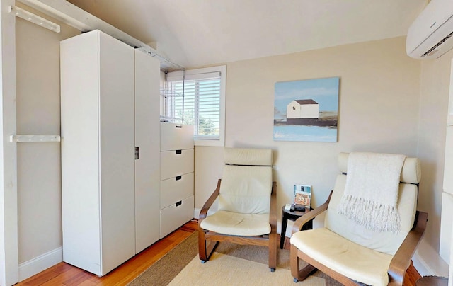 sitting room featuring light hardwood / wood-style floors, vaulted ceiling, and an AC wall unit