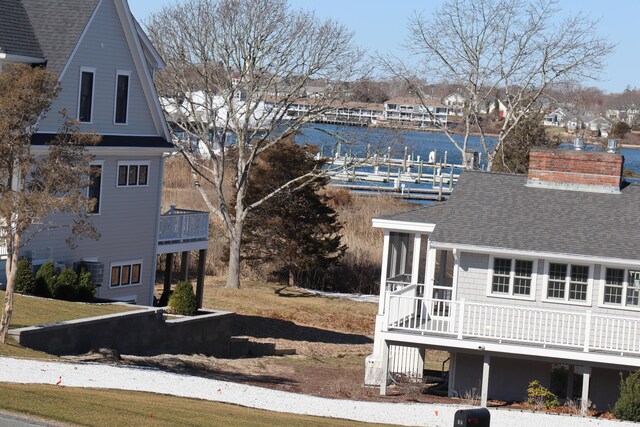 view of side of property featuring a shingled roof, a chimney, a water view, and a sunroom