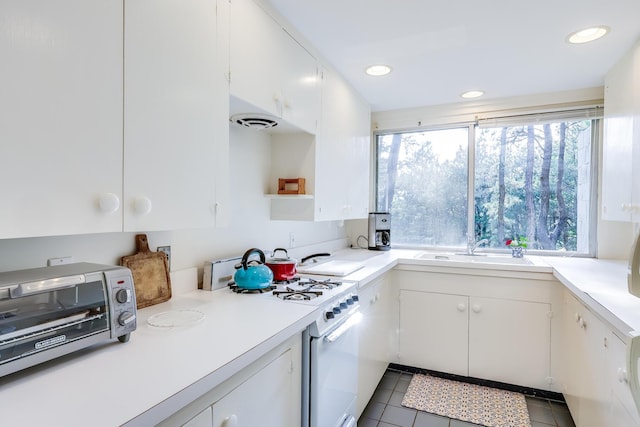 kitchen with white gas range, white cabinetry, sink, and tile patterned flooring