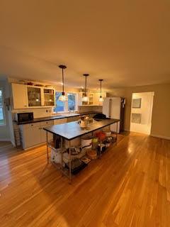 kitchen with a kitchen island, decorative light fixtures, white cabinetry, light hardwood / wood-style floors, and a kitchen breakfast bar