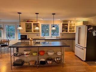 kitchen featuring decorative light fixtures, white refrigerator, light wood-type flooring, cooktop, and a kitchen bar