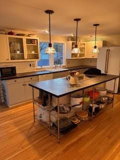 bar with hanging light fixtures, white cabinets, and light wood-type flooring