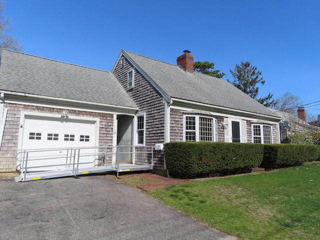 new england style home with driveway, a chimney, a front yard, roof with shingles, and a garage