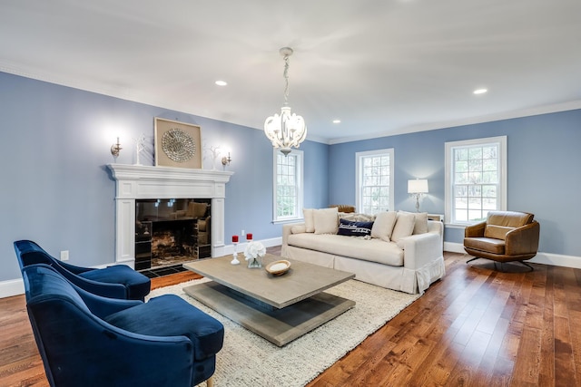 living room with a tile fireplace, hardwood / wood-style floors, an inviting chandelier, and crown molding