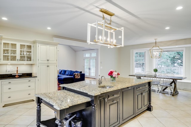 kitchen featuring french doors, sink, decorative light fixtures, dark stone counters, and a kitchen island with sink