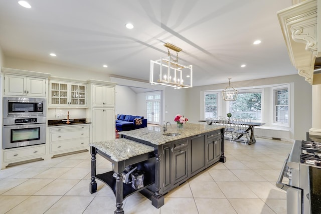 kitchen with light stone countertops, appliances with stainless steel finishes, hanging light fixtures, white cabinets, and sink