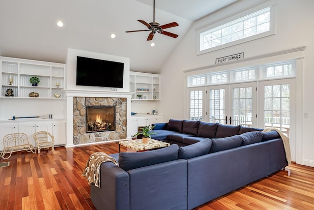 living room featuring high vaulted ceiling, plenty of natural light, a stone fireplace, and light wood-type flooring