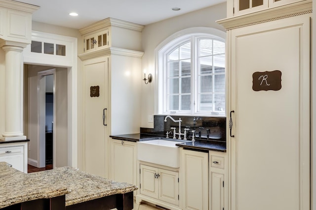 kitchen with decorative columns, cream cabinets, sink, and backsplash