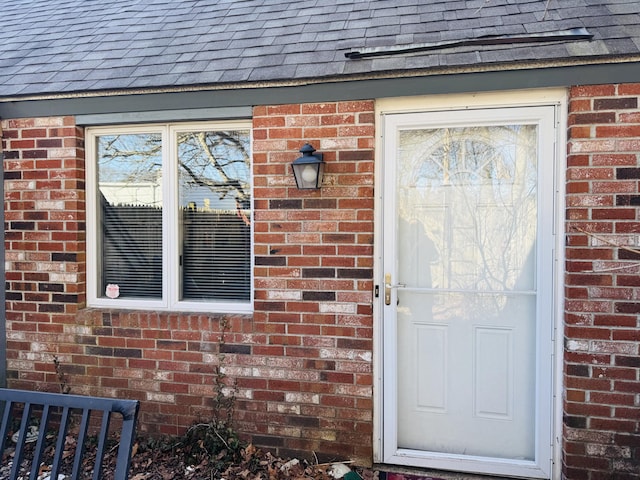 entrance to property with a shingled roof and brick siding