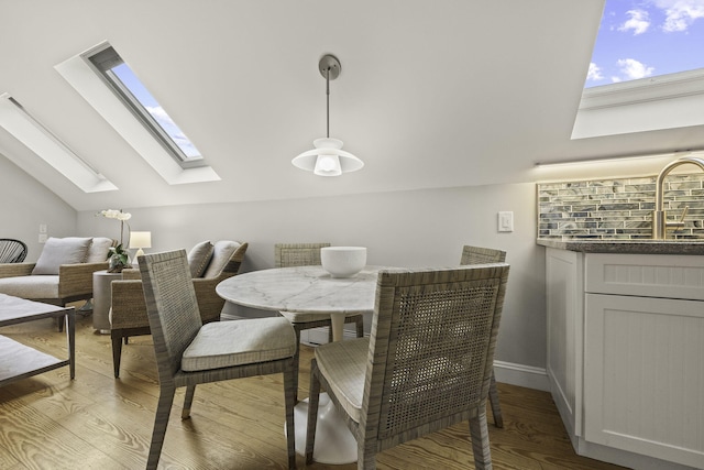 dining space with sink, light wood-type flooring, and vaulted ceiling