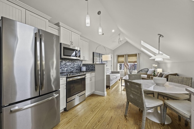 kitchen with appliances with stainless steel finishes, tasteful backsplash, white cabinetry, vaulted ceiling with skylight, and pendant lighting