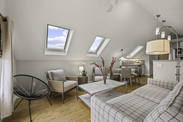 living area featuring ceiling fan, vaulted ceiling with skylight, and light hardwood / wood-style flooring