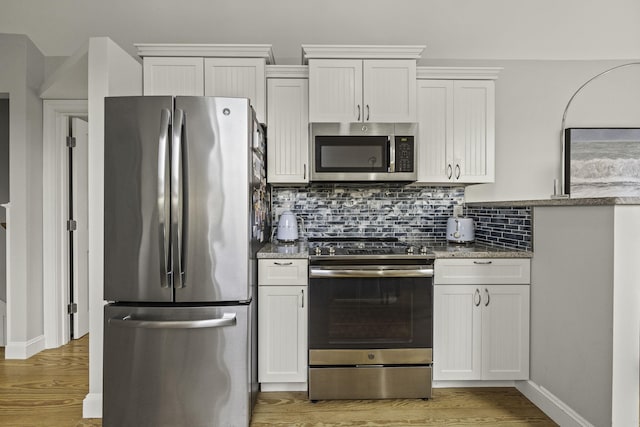 kitchen with white cabinets, light stone counters, appliances with stainless steel finishes, and wood-type flooring