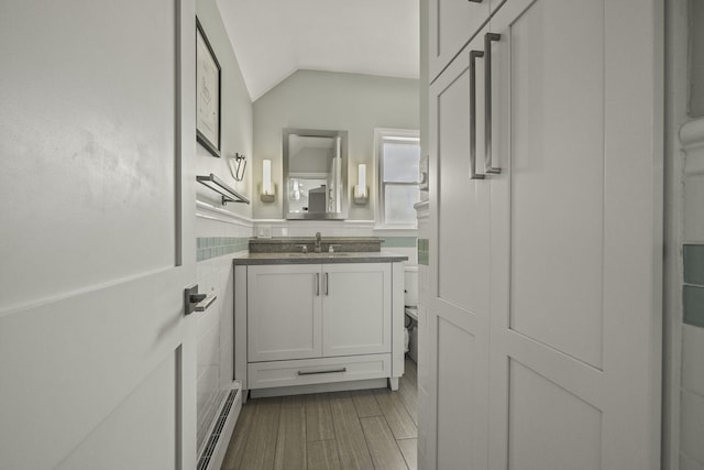 bathroom featuring hardwood / wood-style flooring, tile walls, a baseboard radiator, vanity, and lofted ceiling