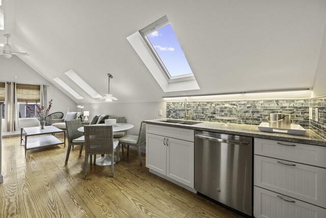 kitchen with vaulted ceiling with skylight, sink, backsplash, hanging light fixtures, and stainless steel dishwasher