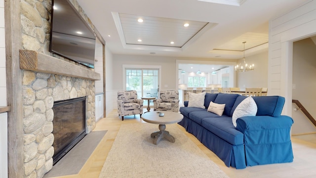 living room featuring a stone fireplace, an inviting chandelier, a tray ceiling, and light hardwood / wood-style floors