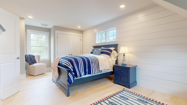 bedroom with light hardwood / wood-style floors, wooden walls, and a closet