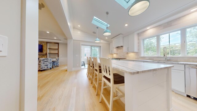 kitchen with a kitchen island, white cabinetry, vaulted ceiling with skylight, and decorative light fixtures