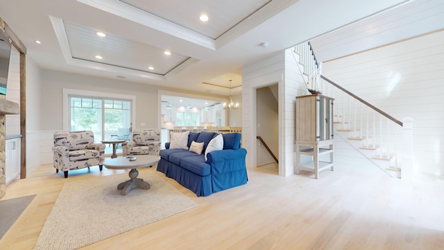 living room with light hardwood / wood-style floors, crown molding, a raised ceiling, and a notable chandelier