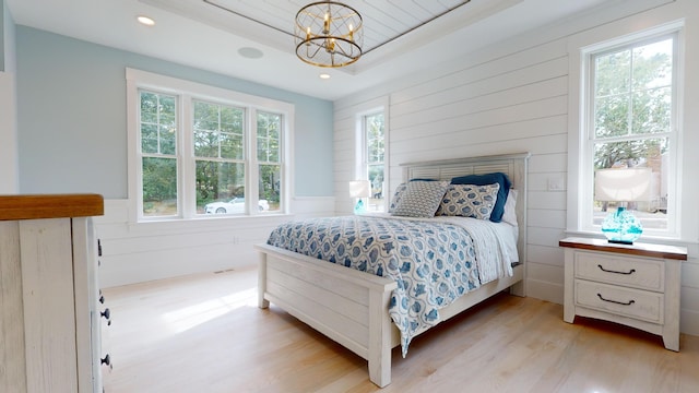 bedroom featuring multiple windows, light hardwood / wood-style flooring, a notable chandelier, and a raised ceiling