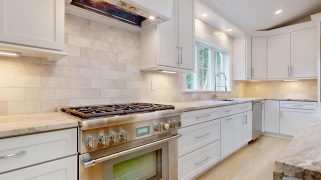 kitchen with sink, white cabinets, wall chimney range hood, and stainless steel appliances