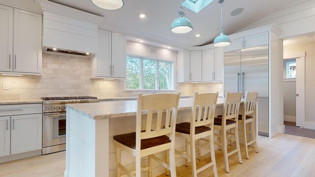 kitchen featuring vaulted ceiling with skylight, white cabinets, decorative light fixtures, light stone counters, and stainless steel range