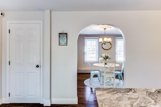dining area featuring arched walkways, dark wood finished floors, a baseboard heating unit, and a chandelier
