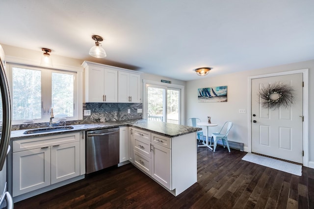 kitchen featuring appliances with stainless steel finishes, a peninsula, a sink, white cabinets, and dark wood-style flooring