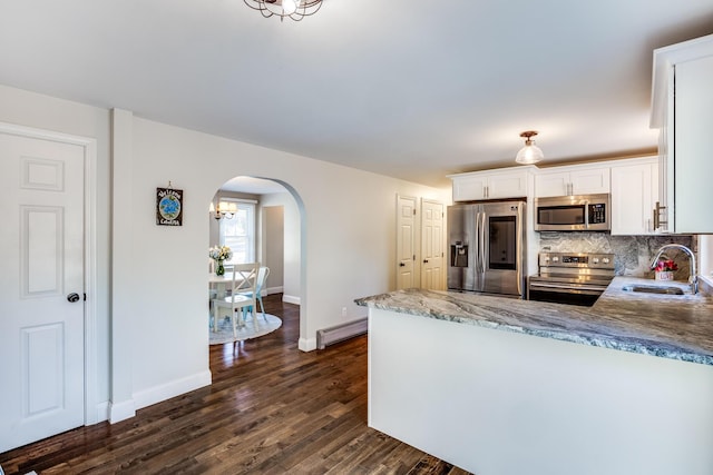 kitchen with appliances with stainless steel finishes, a sink, a baseboard radiator, arched walkways, and white cabinets