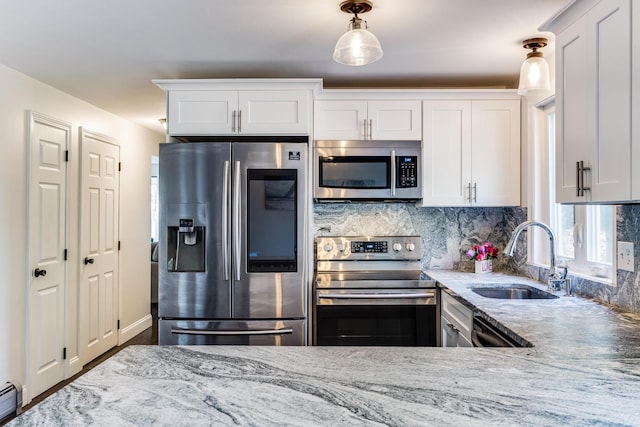 kitchen with stainless steel appliances, a sink, light stone counters, tasteful backsplash, and white cabinets