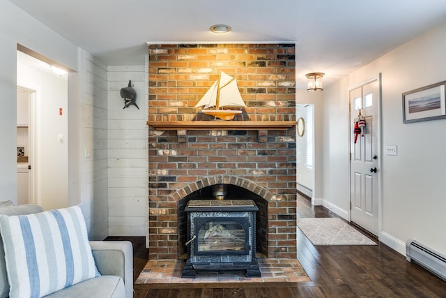 living area featuring a baseboard heating unit, a wood stove, wood finished floors, and baseboards