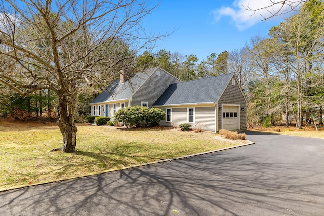 view of property exterior with an attached garage, asphalt driveway, a yard, a shingled roof, and a chimney
