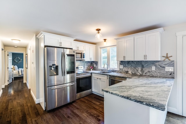 kitchen with appliances with stainless steel finishes, a sink, a peninsula, and dark wood-style flooring