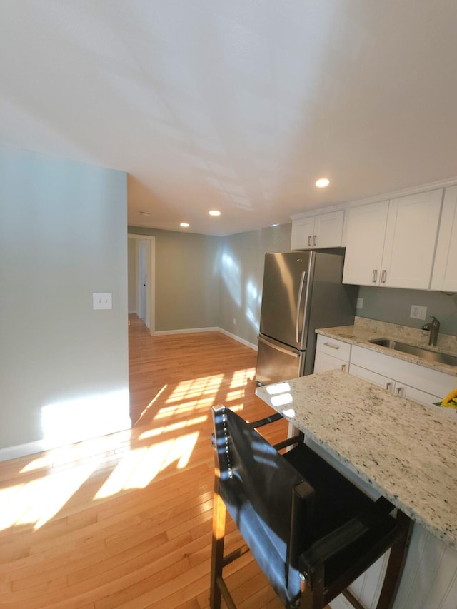 kitchen featuring sink, stainless steel fridge, a breakfast bar, white cabinetry, and light hardwood / wood-style floors