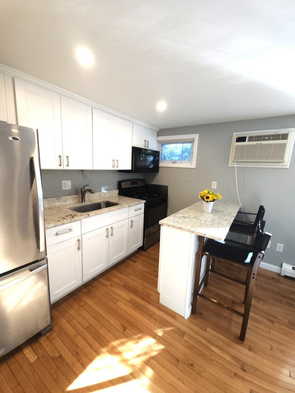 kitchen with sink, white cabinetry, light wood-type flooring, an AC wall unit, and appliances with stainless steel finishes